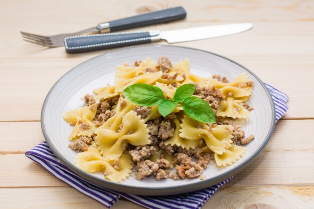 Ready-to-eat pasta navy with minced meat  and basil leaves on a plate and cutlery on a wooden table. Russian cuisine