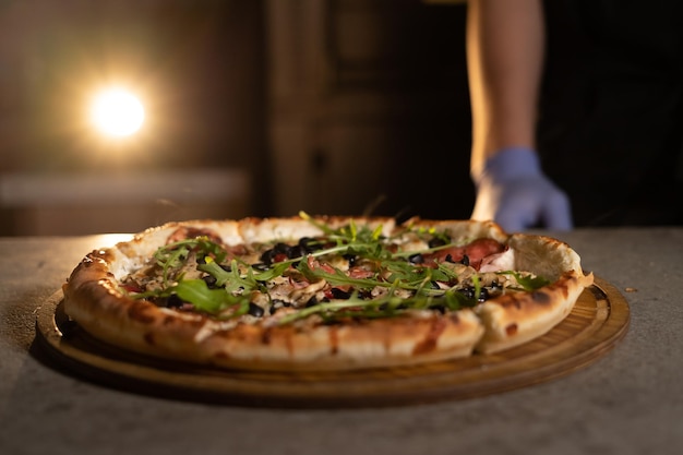 Ready hot Italian pizza lies on a wooden board on the table in the kitchen. Lighted oven in the background. Ready meal for dinner.