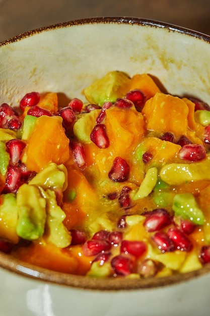 Photo ready-made fruit salad with avocado, mango and pomegranate in bowl in the kitchen.