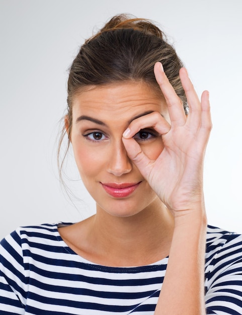 Photo ready for the masquerade ball shot of a beautiful young woman using her fingers to make a ring around her eye