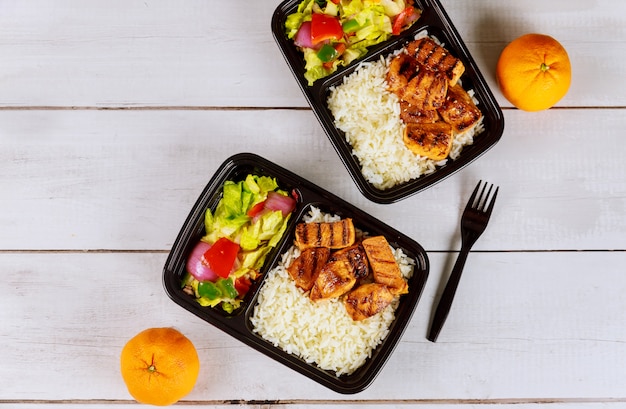 Ready meal to eat on food container with drink and orange.