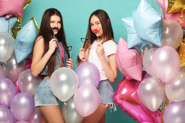 Ready for party Two girls in stylish summer outfit paper glasses and air balloons having fun and celebrate birthday