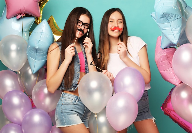 Foto pronto per la festa due ragazze in elegante abito estivo occhiali di carta e palloncini d'aria divertendosi e festeggiano il compleanno