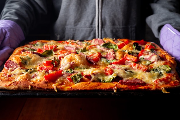 Ready pizza in hands on a baking sheet in hands in the kitchen at home