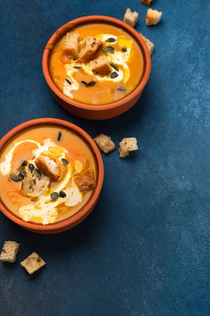 Zuppa pronta di crema di zucca con panna e crostini due porzioni su sfondo blu vista dall'alto