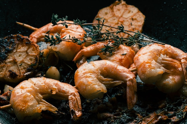 Ready roasted shrimps with garlic cloves on the pan. Thyme sprigs on the top