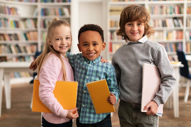 Ready for school Portrait of diverse kids posing with notebooks looking and smiling at camera standing in classroom