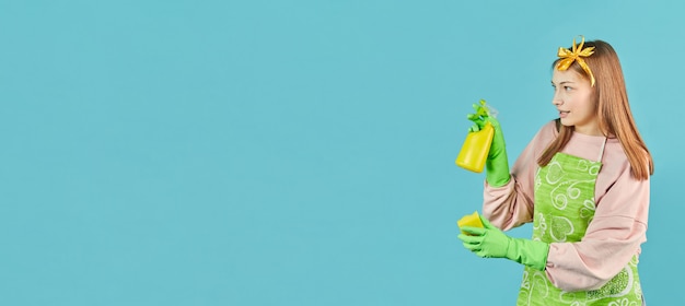 Photo ready for spring-cleaning. portrait of joyful girl with household supplies in hands over blue wall. young woman hold household cleaning product and spray bottles.