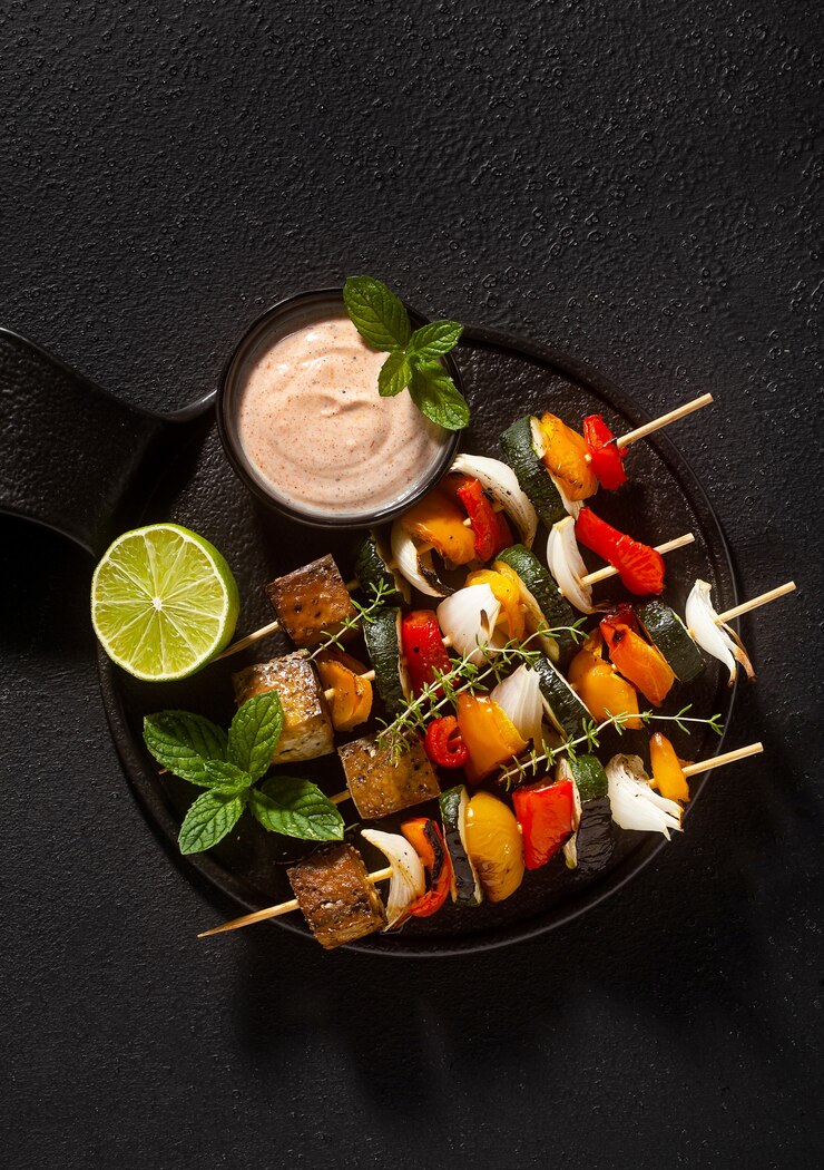Photo ready vegan kebabs of vegetables and smoked tofu with cashew sauce and smoked paprika on a black