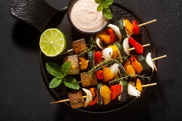 Ready vegan kebabs of vegetables and smoked tofu with cashew sauce and smoked paprika on a black