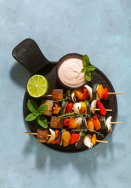 Ready vegan kebabs of vegetables and smoked tofu with cashew sauce and smoked paprika on a blue