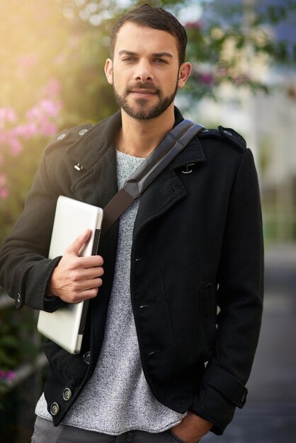 Ready for whatever the day holds Shot of a handsome young man standing outdoors and holding a laptop