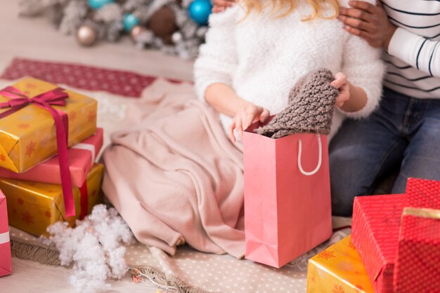 Foto pronto per l'inverno. primo piano di un caldo cappello lavorato a maglia che viene messo fuori dal sacchetto di carta da una donna giovane e carina