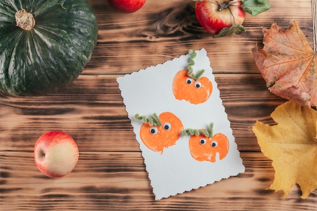 りんごのかぼちゃのプリントが入った既製のハロウィン カードがりんごの横にあり、木の表面に紅葉します。トップ ビュー