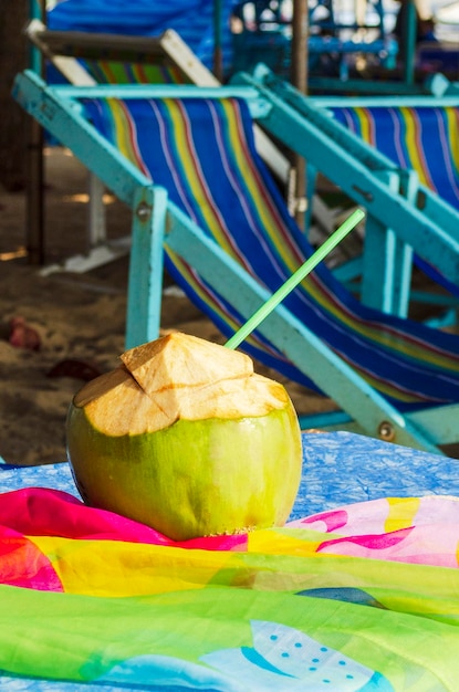 Готовый напиток из кокосового свежего зеленого кокоса с шезлонгами на пляже