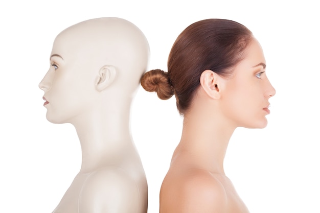 Real and artificial. Side view of beautiful young shirtless woman standing her back to the mannequin and looking away while isolated on white background