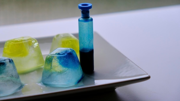 Real colored ice cubes on a white tray with a bottle of blue ink