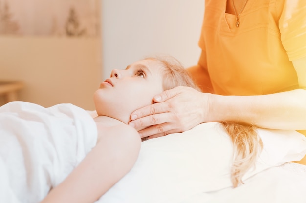 Le mani di un vero dottore osteopata fanno terapia fisiologica ed emotiva per una bambina di otto anni. sessione di trattamento di osteopatia pediatrica. medicina alternativa. prendersi cura della salute del bambino. bagliore