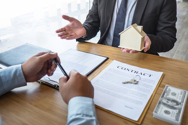 Real estate agent are presenting home loan and giving house, keys to customer after signing contract to buy house with approved property application form.