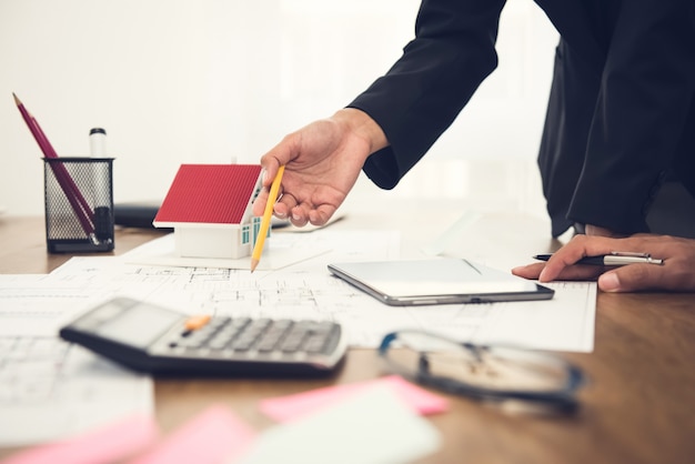 Real estate agent discussing work with blueprints and house model on the table