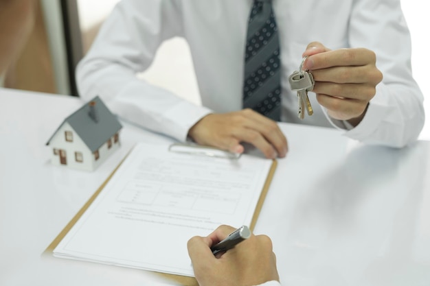 Photo real estate agent giving house keys to client after signing home loan contract