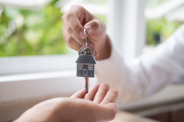 Mano dell'agente immobiliare che fornisce le chiavi di una casa per alloggiare il compratore.