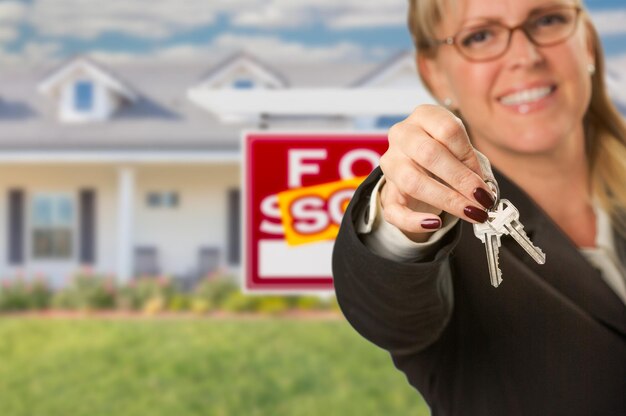 Photo real estate agent handing over new house keys with sold sign behind