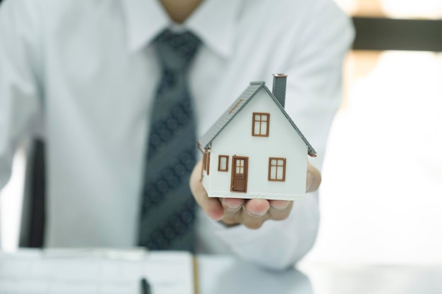 Real estate agent holding house model and keys to consult client