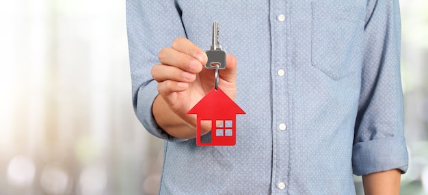 Agente immobiliare che tiene chiave con piccola casa rossa