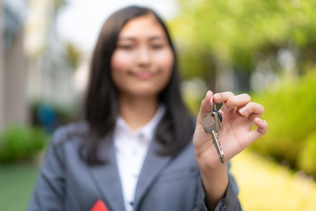 Агент по недвижимости или женщина-риэлтор улыбается и держит красный файл с ключом от дома