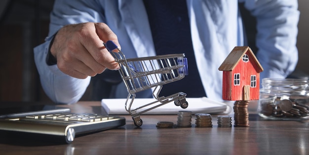 Real estate agent showing house model shopping cart and coins
