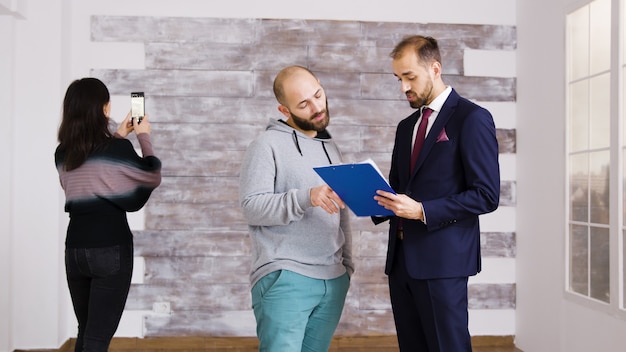 Real estate agent talking with client in empty apartment. Woman taking pictures in empty apartment.