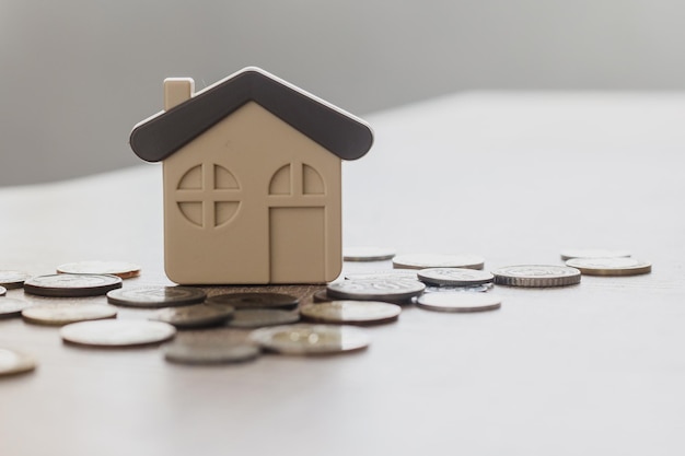 Концепция недвижимости и покупки дома, сложенная из множества монет на деревянном столе с модельным домом, экономящая деньги