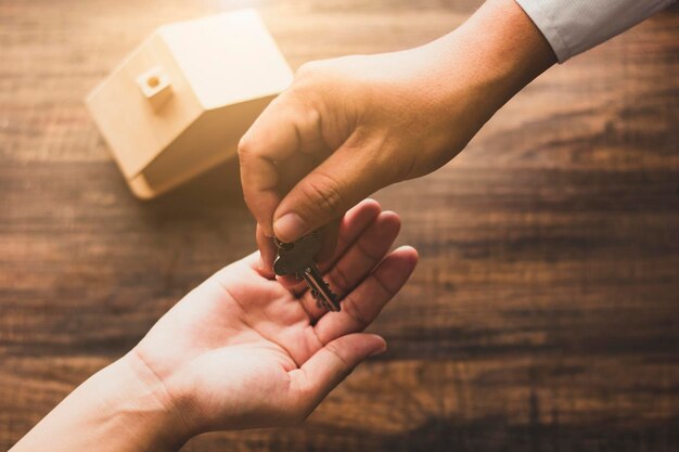 Photo real estate concept home agency banker give house key to owner or buyer on wood table in vintage tone