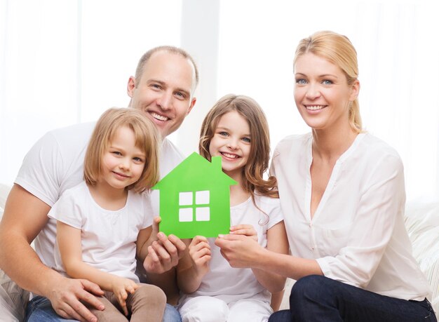 real estate, family, children and home concept - smiling parents and two little girls holding green house