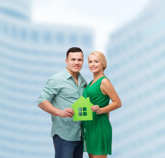 real estate, family and couple concept - smiling couple holding green paper house