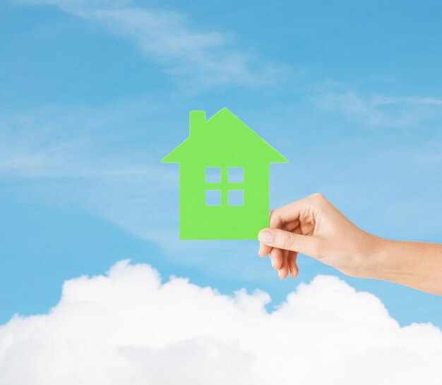 real estate and family home concept - closeup picture of female hand holding green paper house