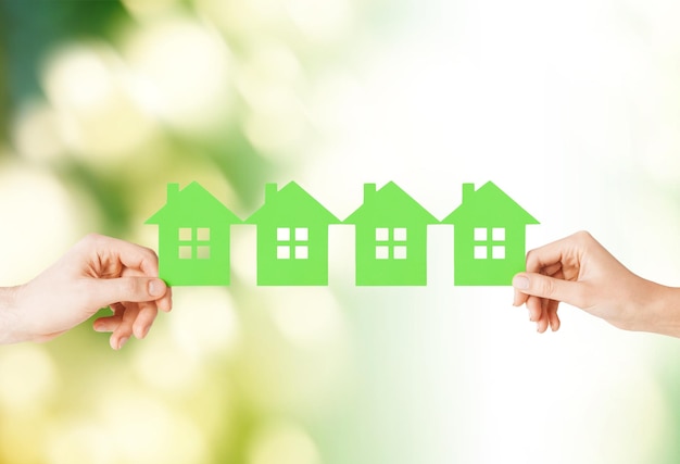 real estate and family home concept - closeup picture of male and female hands holding many green paper houses