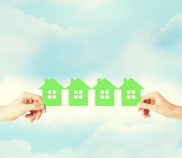 real estate and family home concept - closeup picture of male and female hands holding many green paper houses