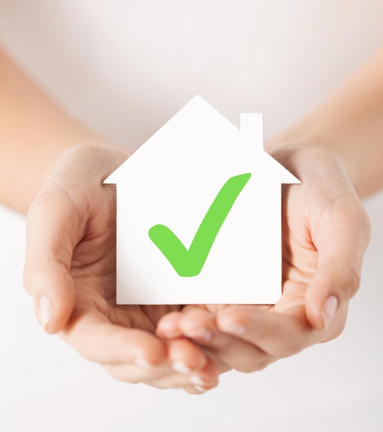 부동산 및 가족 주택 개념 - 녹색 확인 표시가 있는 종이 집을 들고 있는 손