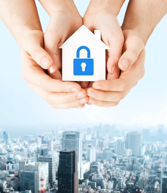 real estate and family home security concept - closeup picture of male and female hands holding white paper house with blue lock