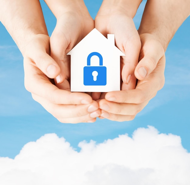 Photo real estate and family home security concept - closeup picture of male and female hands holding white paper house with blue lock