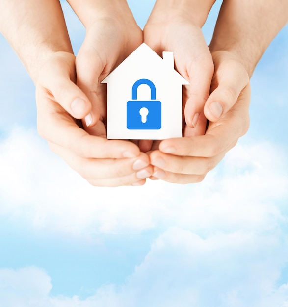 real estate and family home security concept - closeup picture of male and female hands holding white paper house with blue lock