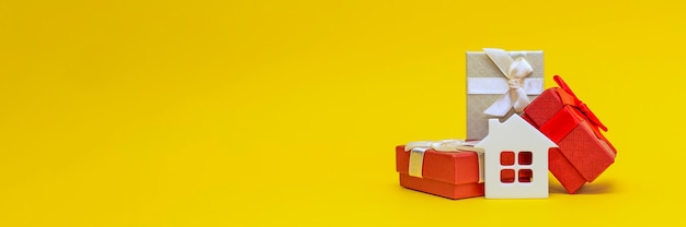 Real estate gift, home gift. White toy house in a gift box on a yellow background. Postcard for printing, banner with place for text.