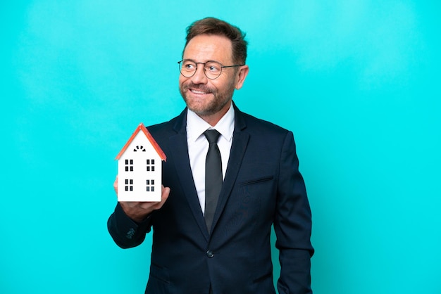 Фото Агент по недвижимости среднего возраста мужчина изолирован на синем фоне, думая об идее, глядя вверх
