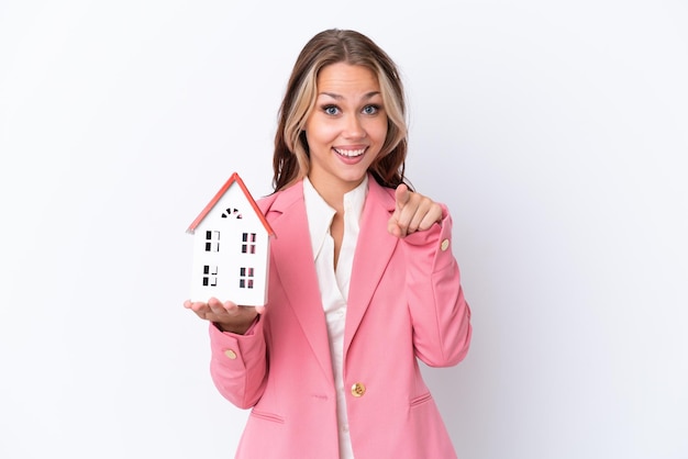 Real estate Russian agent holding a toy house isolated on white background surprised and pointing front