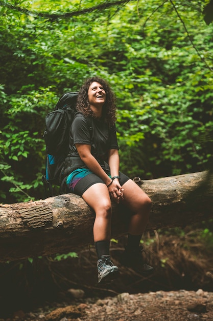 Viandante reale e naturale che riposa su un albero caduto e sorridente.