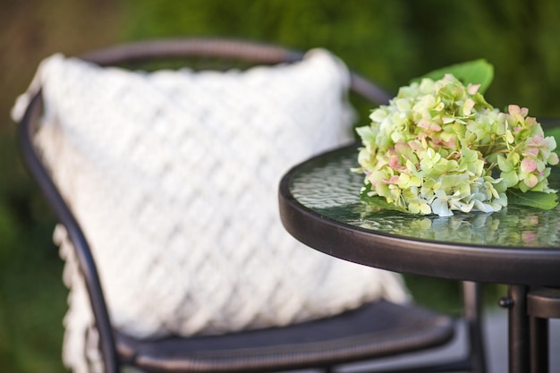 Real photo of a modern garden chair withmacrame pillow standing on a wooden deck in the garden of a weekend retreat