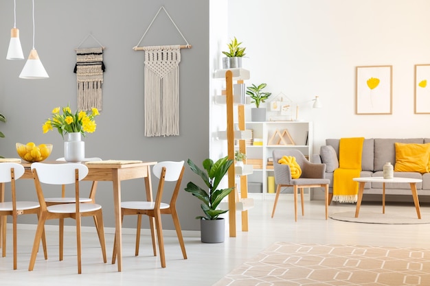 Photo real photo of a spacious home interior with wooden table white chairs and macrame on the wall in dining room and a gray sofa and armchair in the living room