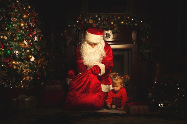 Real Santa Claus is playing with children near the Christmas tree. 